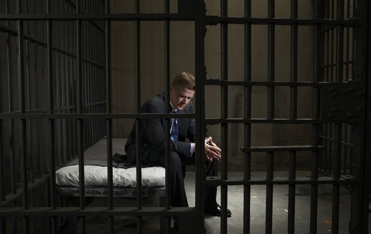 Mature businessman sitting on bed in prison cell