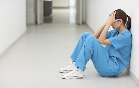 Nurse sitting in a corridor while holding her head